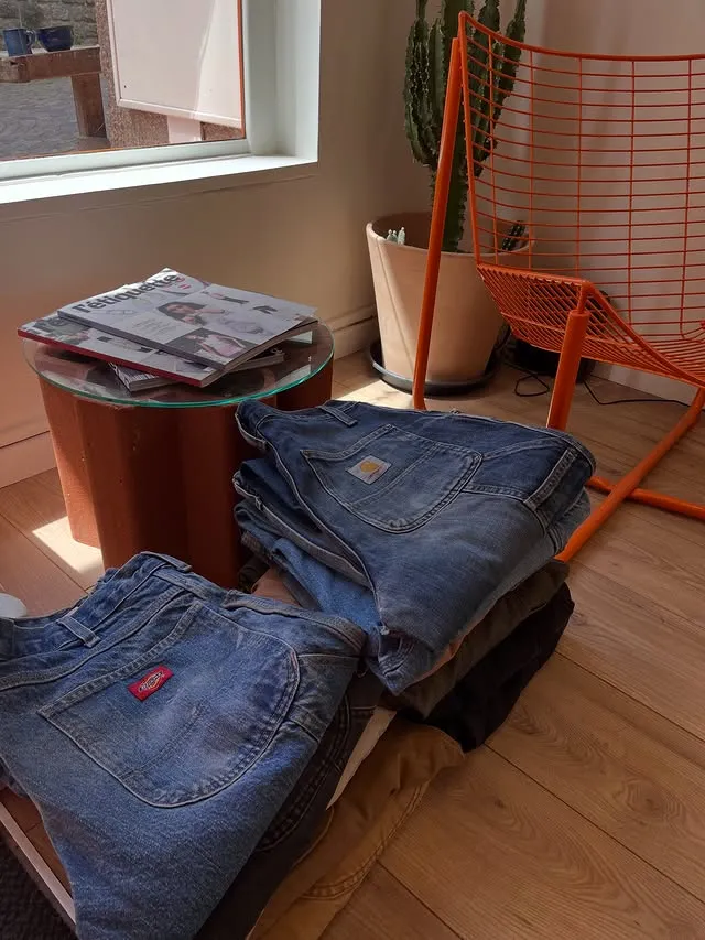 Intérieur de la boutique : jeans pliés sur une table, mobilier orange et sol en bois