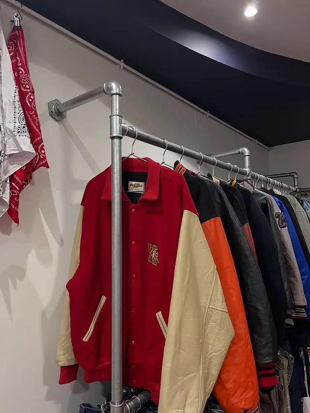 Portant de vestes vintage à l'intérieur de la boutique, dont une veste varsity rouge et crème