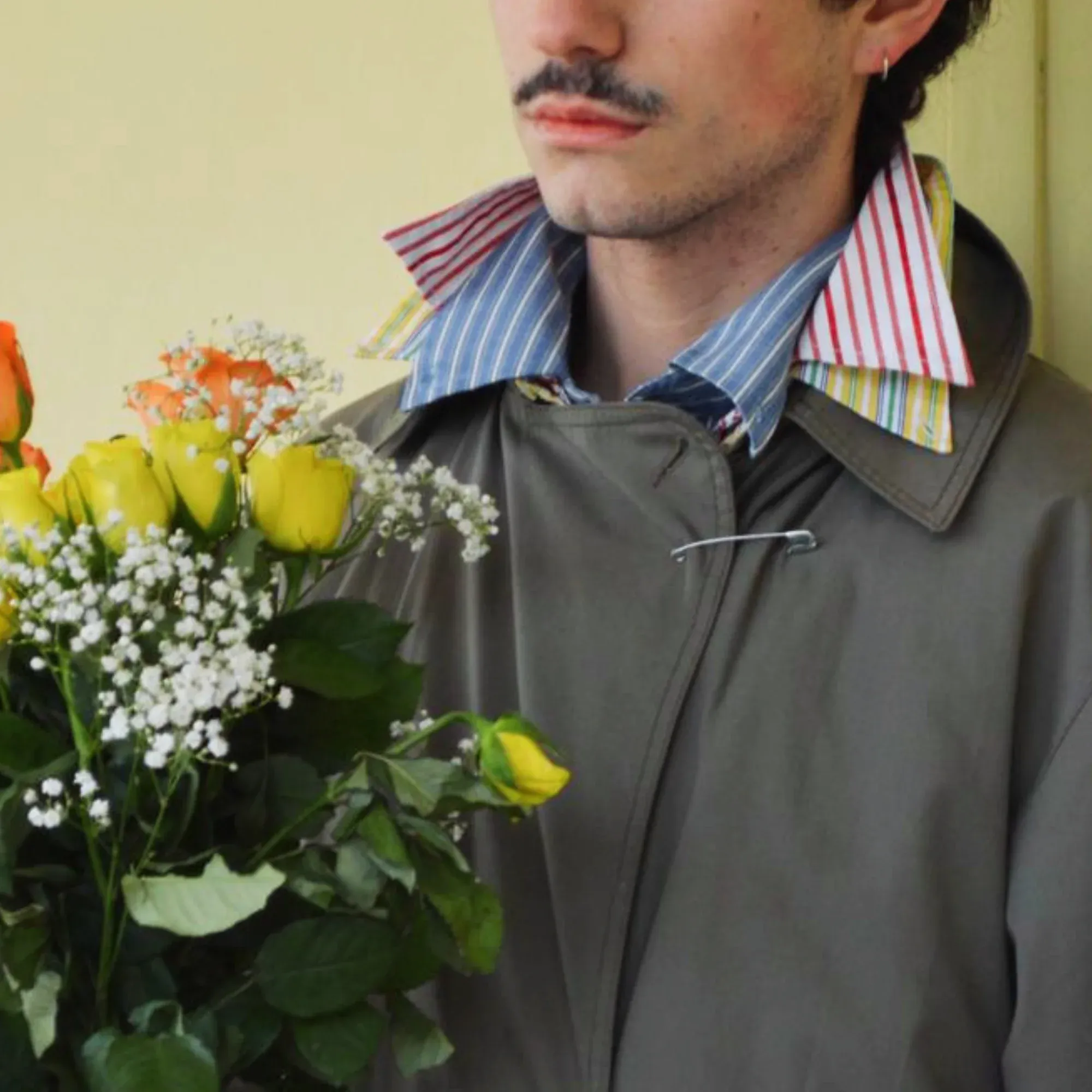 Veste et chemise à col rayé portées devant un bouquet de fleurs